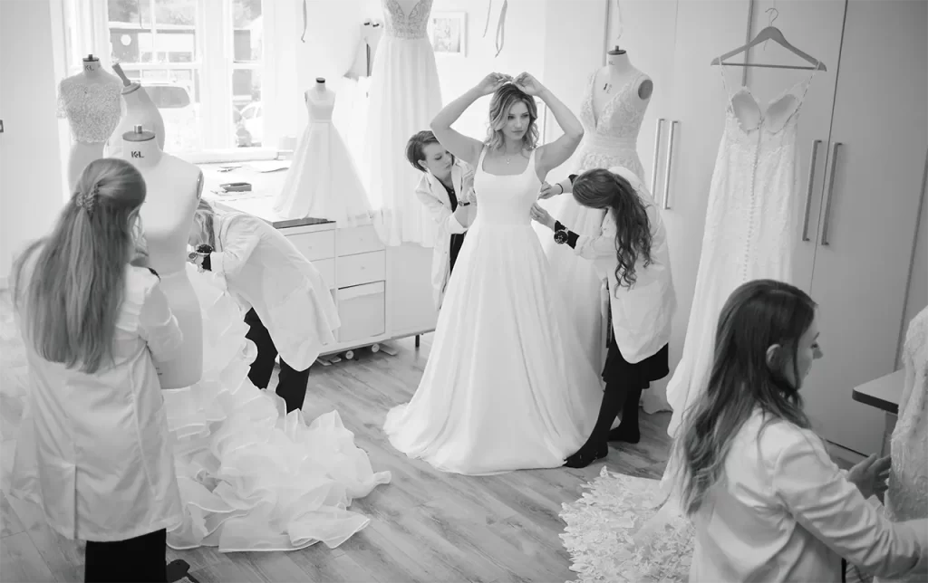 black and white image of a bridal model being fitted for a wedding dress with seamstresses surrounding her.